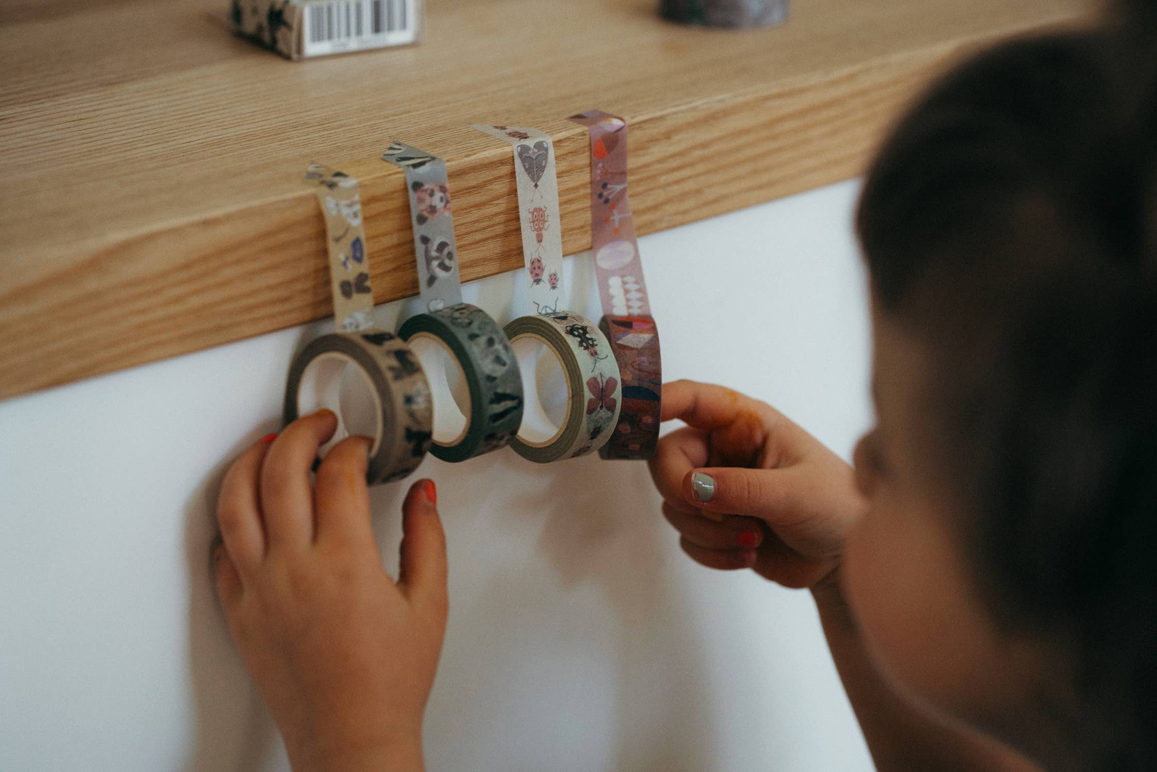 Child arranging colorful washi tape on a wooden board