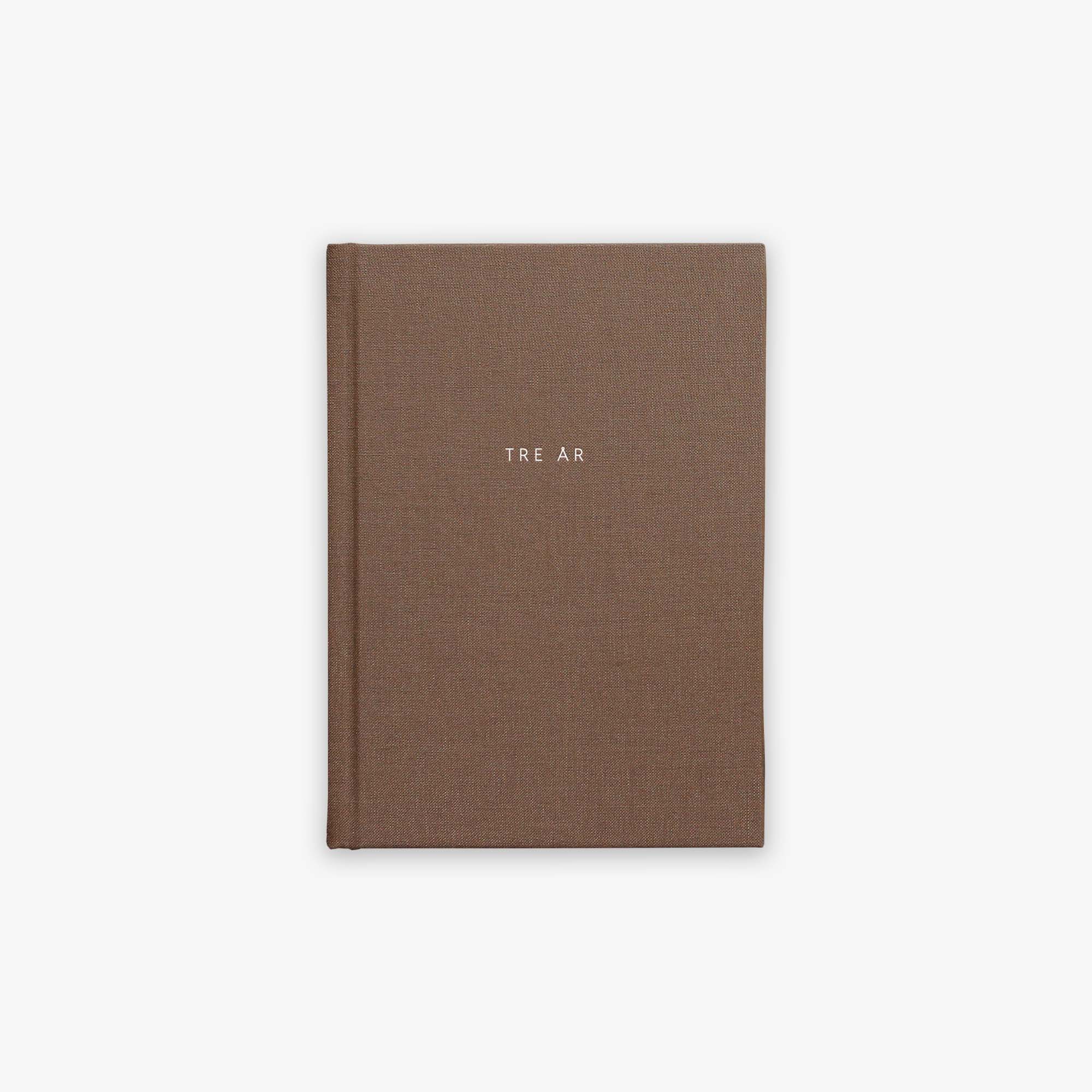 Brown guided journal with 'TRE ÅR' text embossed on the cover on a white background