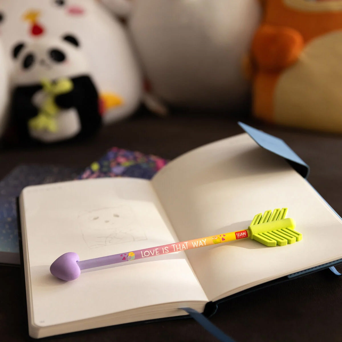 Open notebook with a pencil on a wooden surface, surrounded by plush toys.