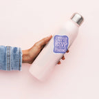 White insulated bottle with a purple 'I would like to RSVP as pending' sticker held by a person wearing denim jeans.