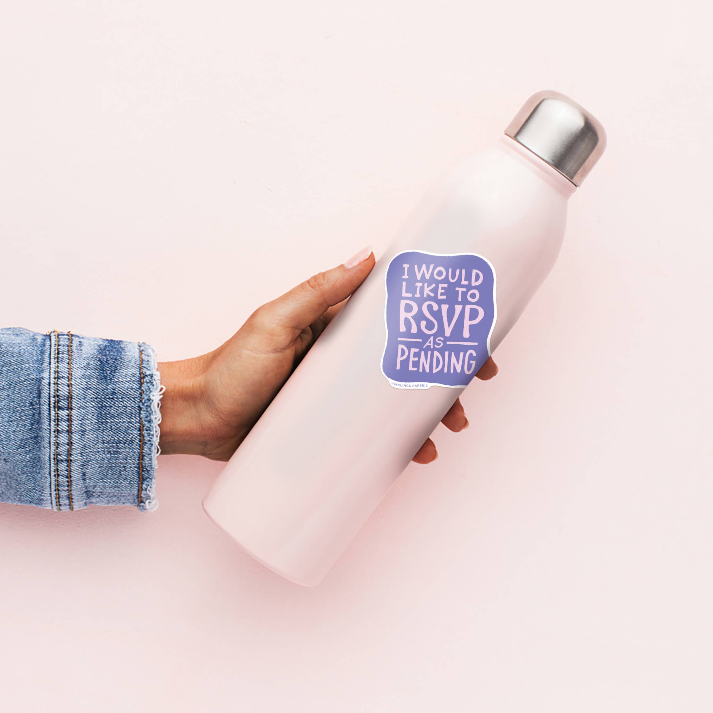 White insulated bottle with a purple 'I would like to RSVP as pending' sticker held by a person wearing denim jeans.