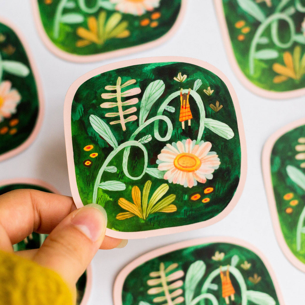 Hand holding a square sticker with nature-themed design on a white background