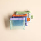 Set of three transparent mesh pouches with colorful zippers on a beige background