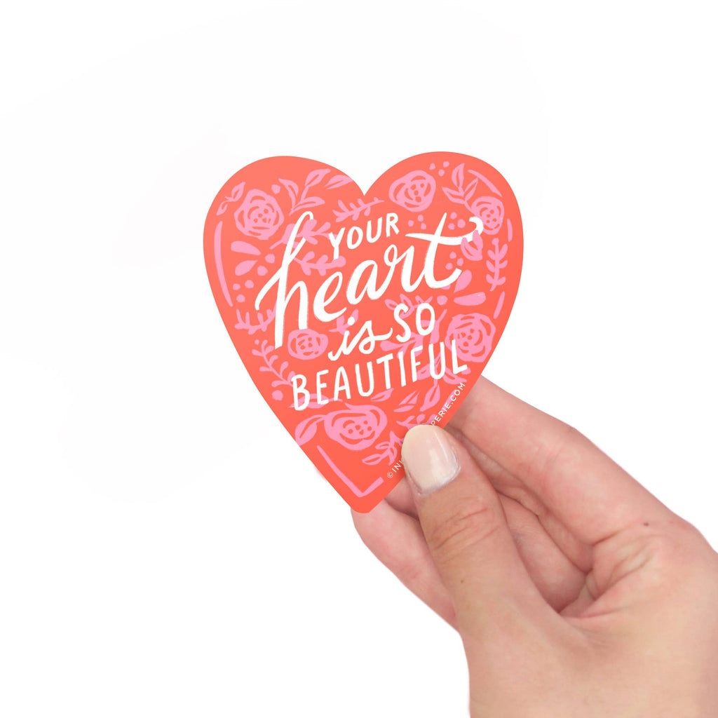 Heart-shaped vinyl sticker with 'Your heart is so beautiful' text held by a hand on a white background
