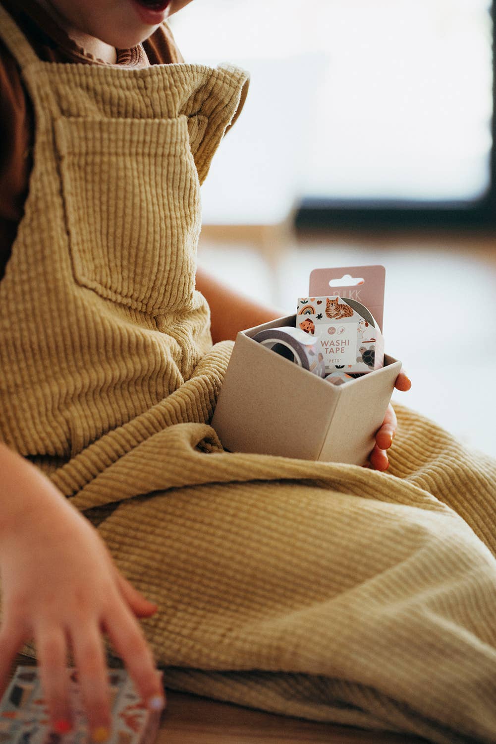 Person wearing yellow bib pants holding a small box with masking tapes.