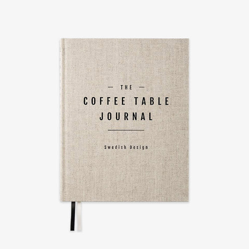 A hardcover journal with a light beige linen-textured cover and black text reading 'THE COFFEE TABLE JOURNAL' and 'Swedish Design'. A black ribbon bookmark is visible at the bottom left, shown on a plain white background.