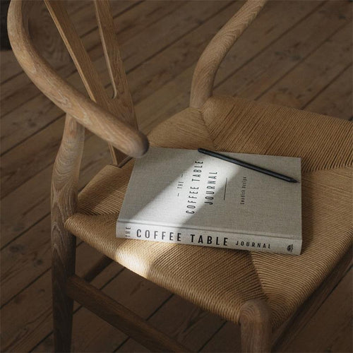 A hardcover notebook with a light beige linen-textured cover and black text reading 'THE COFFEE TABLE JOURNAL' and 'Swedish Design'. A black ribbon bookmark is visible at the bottom left