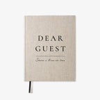 A linen-textured hardcover notebook with black printed text reading 'DEAR GUEST' and 'Share a line or two' on a clean white background.