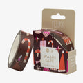 A roll of Nuukk Christmas-themed washi tape next to its cardboard packaging box, featuring festive holiday illustrations like candy canes and snowman hats on a dark brown background.