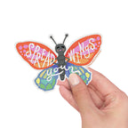 Butterfly-shaped sticker with 'Spread Wings' text held by a hand on a white background