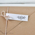 Kraft paper envelope with a white label and decorative plant leaf stamp on a light wooden surface.
