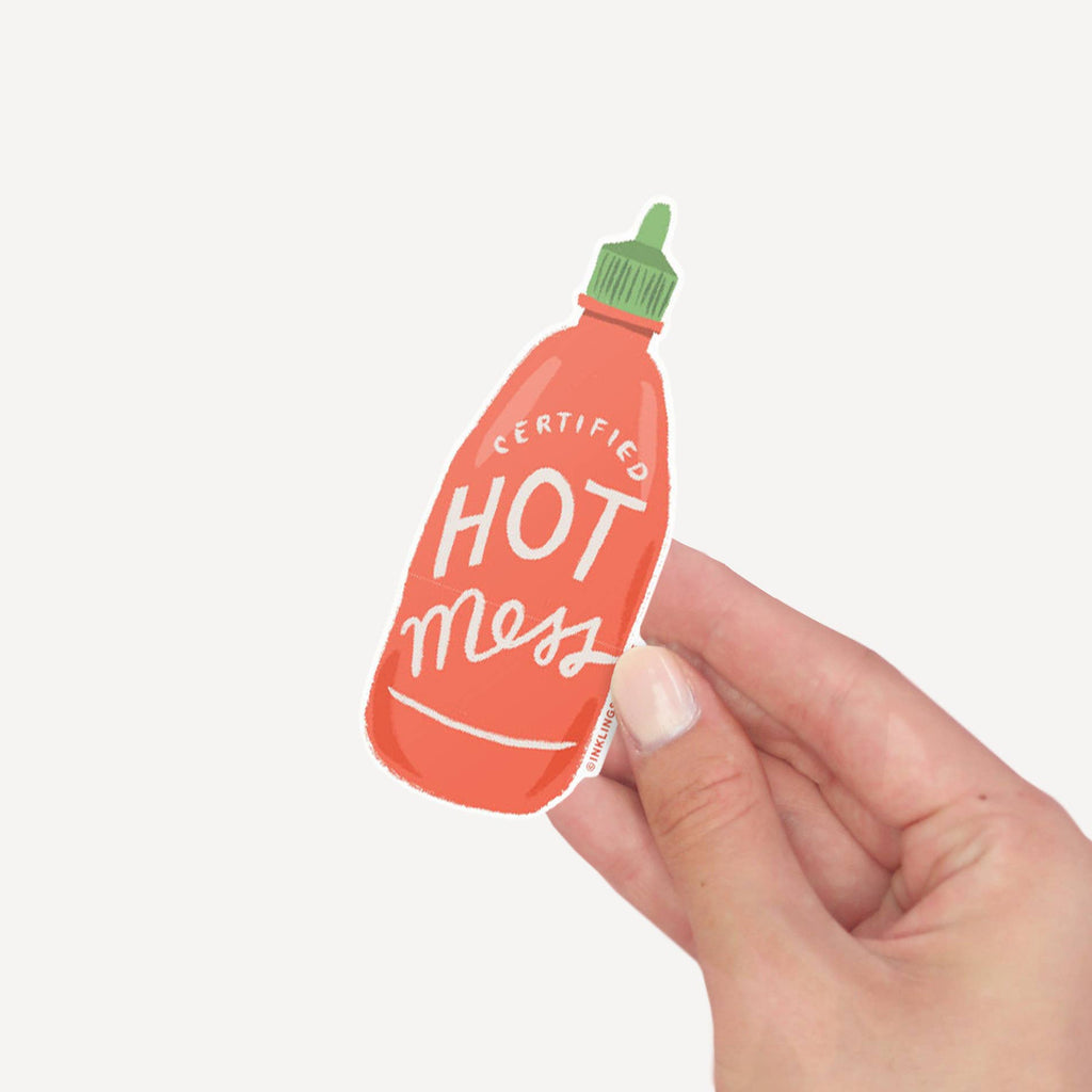 Hand holding a small bottle-shaped vinyl sticker with 'Certified Hot Mess' text on a light gray background