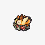 A die-cut sticker featuring a whimsical illustration of an owl with closed eyes, orange wings, and a yellow hat, nestled among green leaves and red berries on a black background.