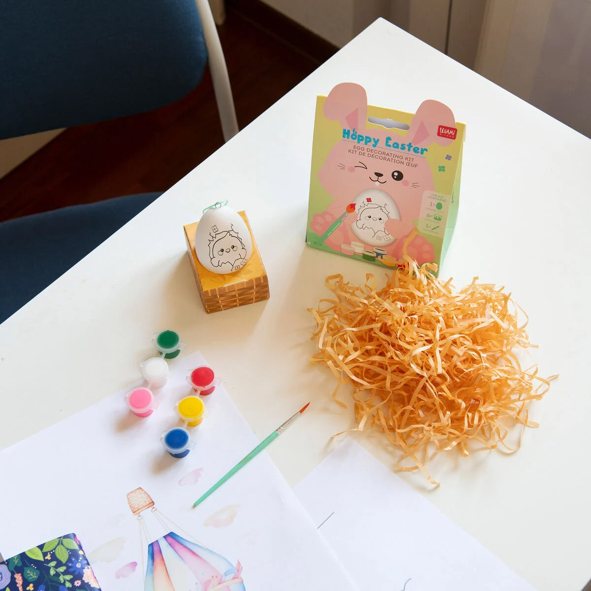 Easter-themed craft supplies including paint, paper, and a box on a table.