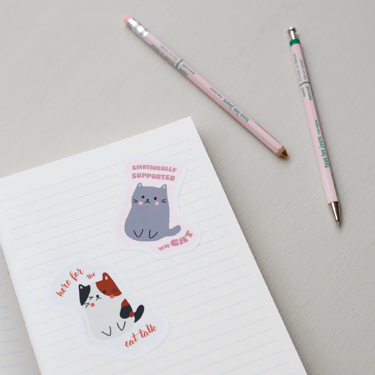 Notebook with cat-themed stickers and two pens on a light gray background