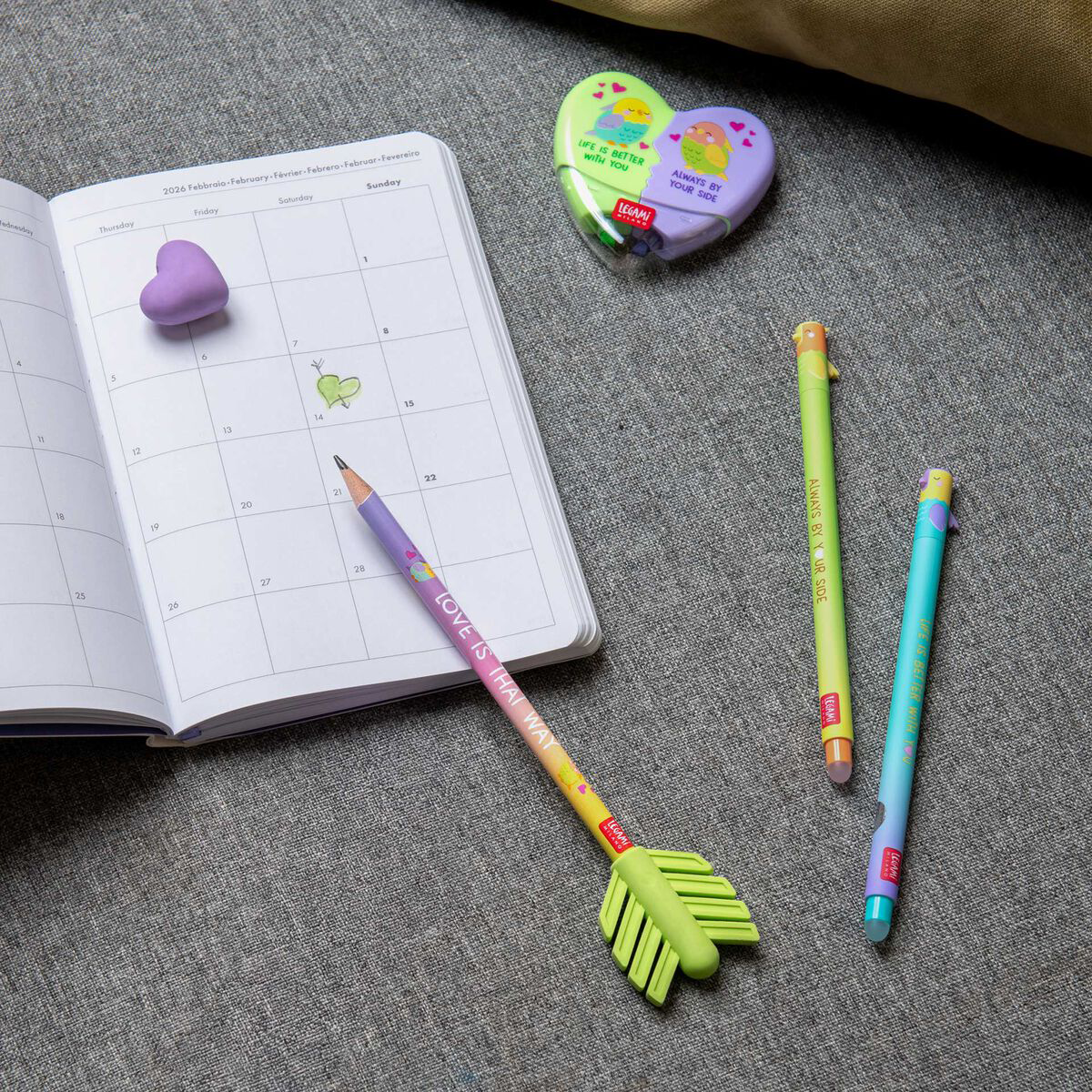 Colorful stationery items including pens and a small notebook on a textile gray surface.