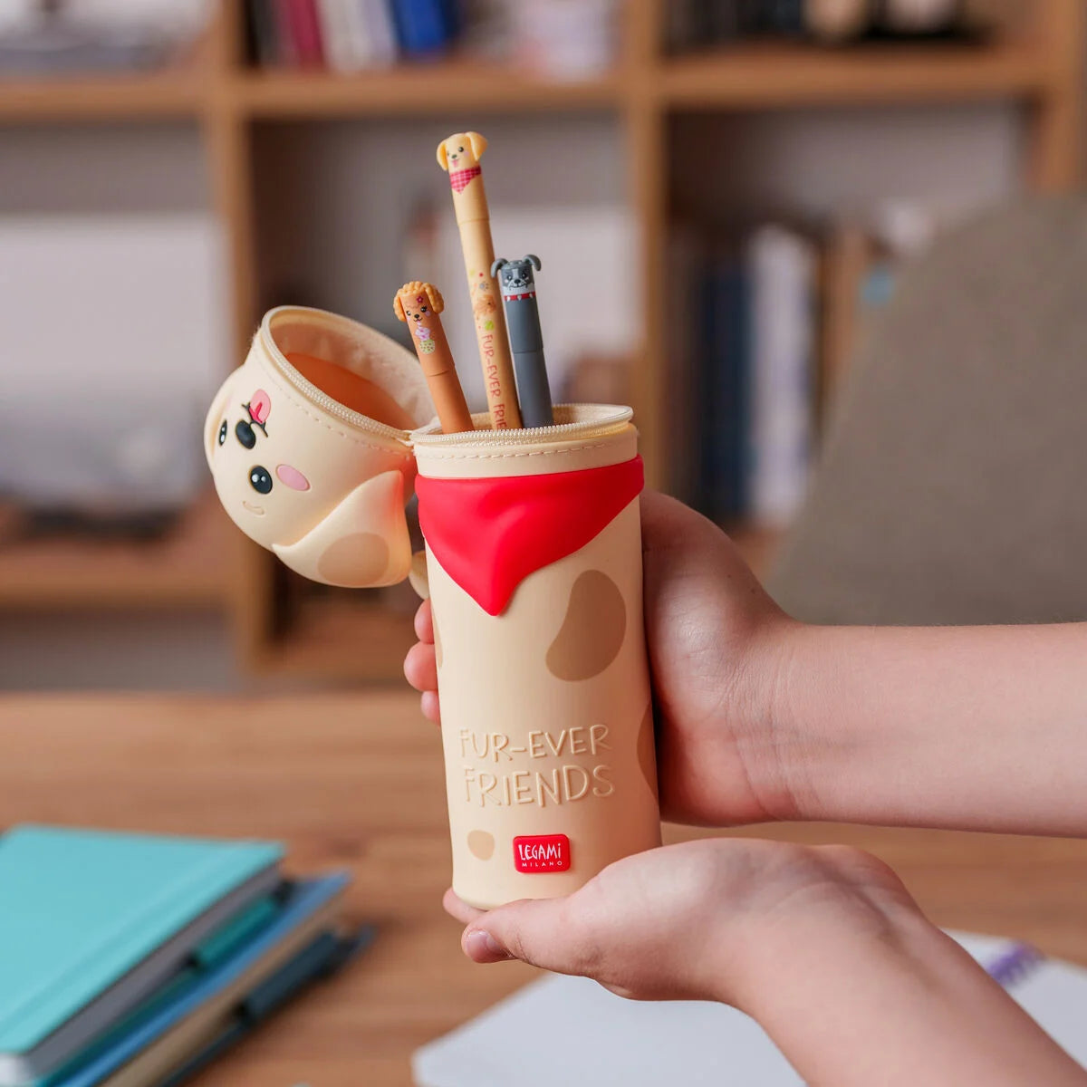 Person holding a pen holder with cartoon designs on a desk