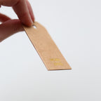 Hand holding a brown gift tag with gold 'Merry xmas' text on a white background
