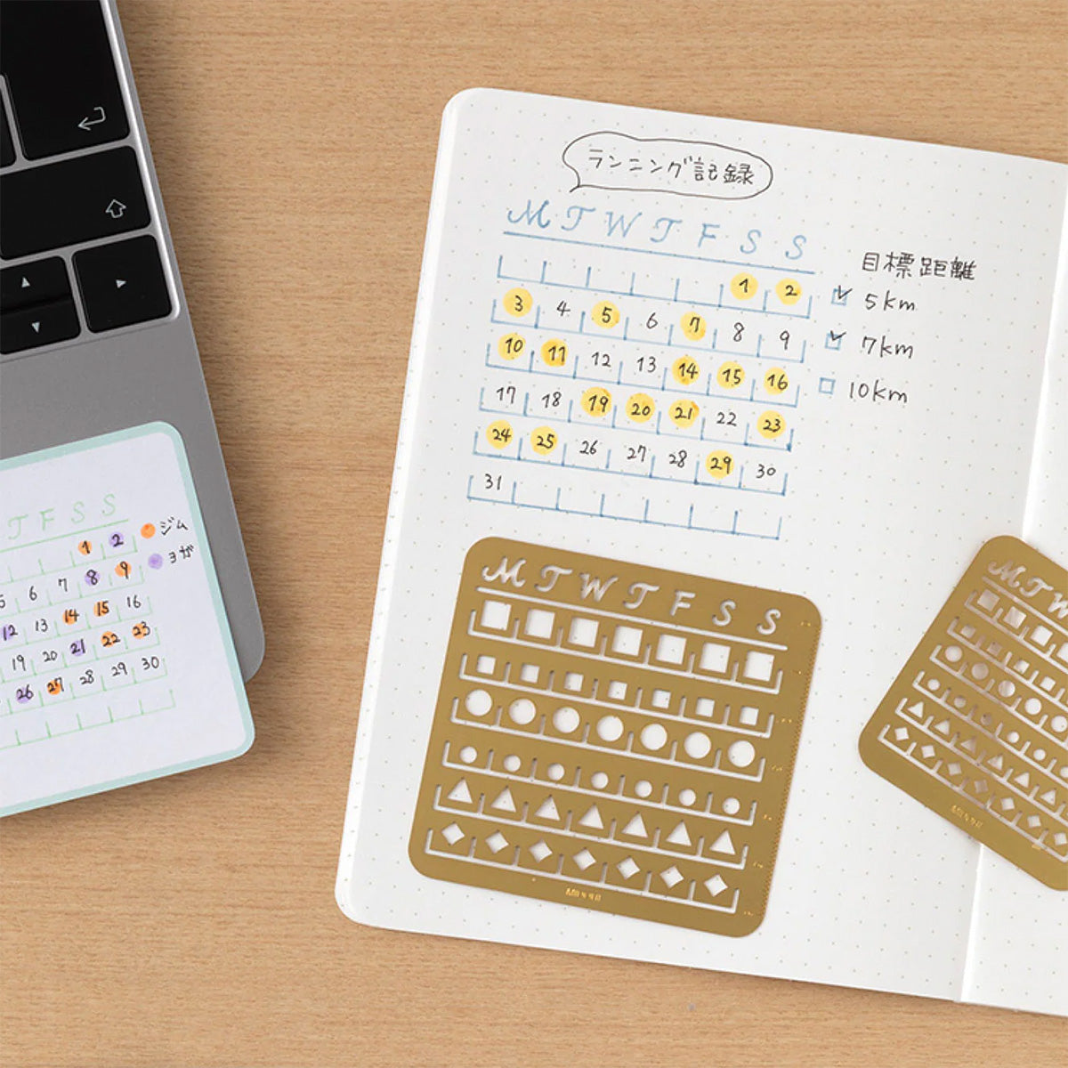 Notebook with calendar stencils on a wooden surface next to a laptop.