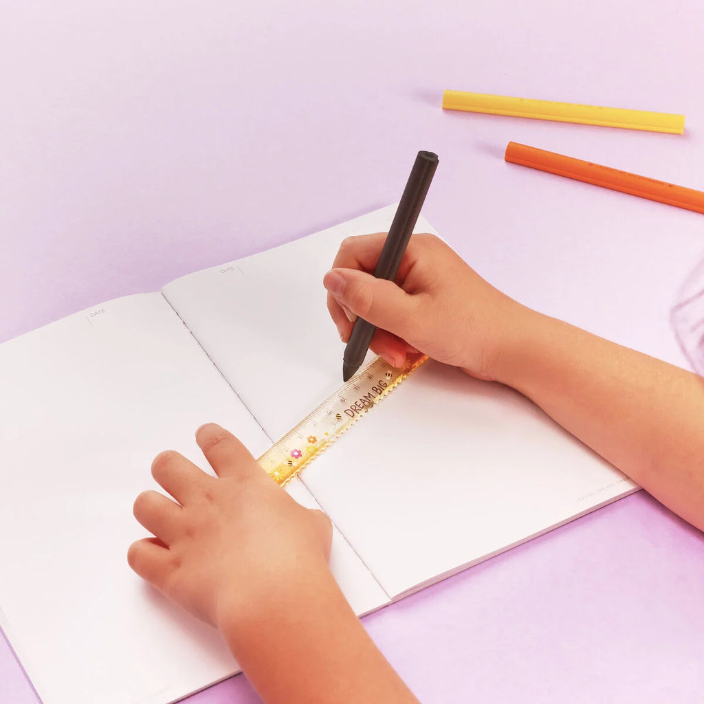 Child's hands holding a pen and ruler on a white sheet of paper with colorful markers on a light purple background