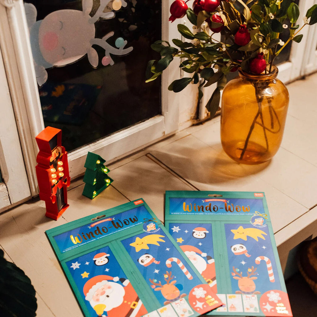 Window stickers with Christmas designs on a tiled floor next to a vase with flowers.