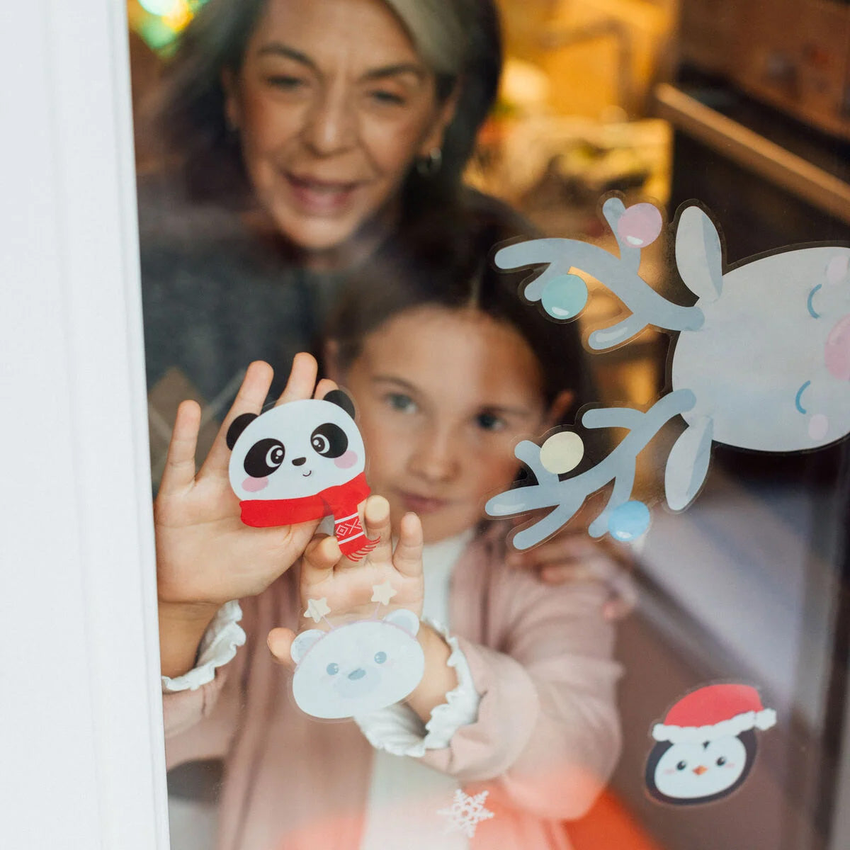 Two children looking through a window with festive Christmas stickers on it.