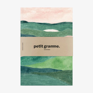 Notebook with green landscape design and 'petit gramme' branding on a white background