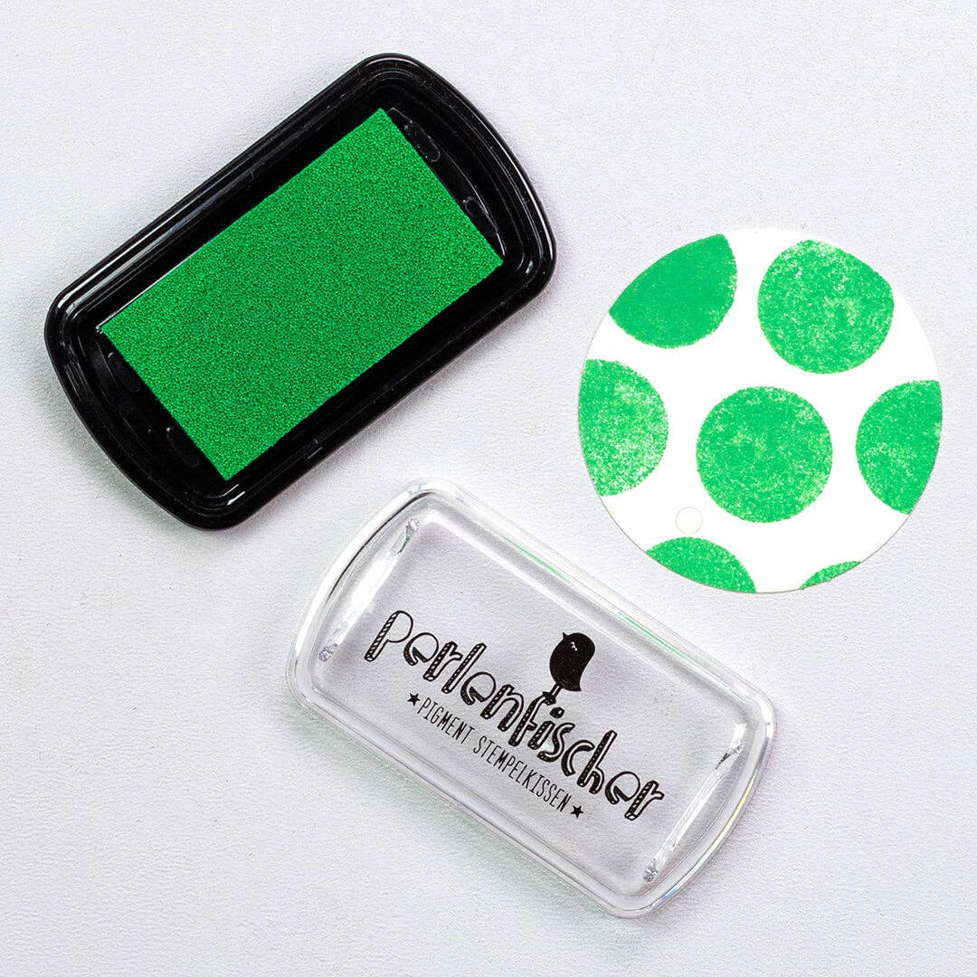 Green ink pad, clear stamp with green polka dots, and black ink pad on a white background