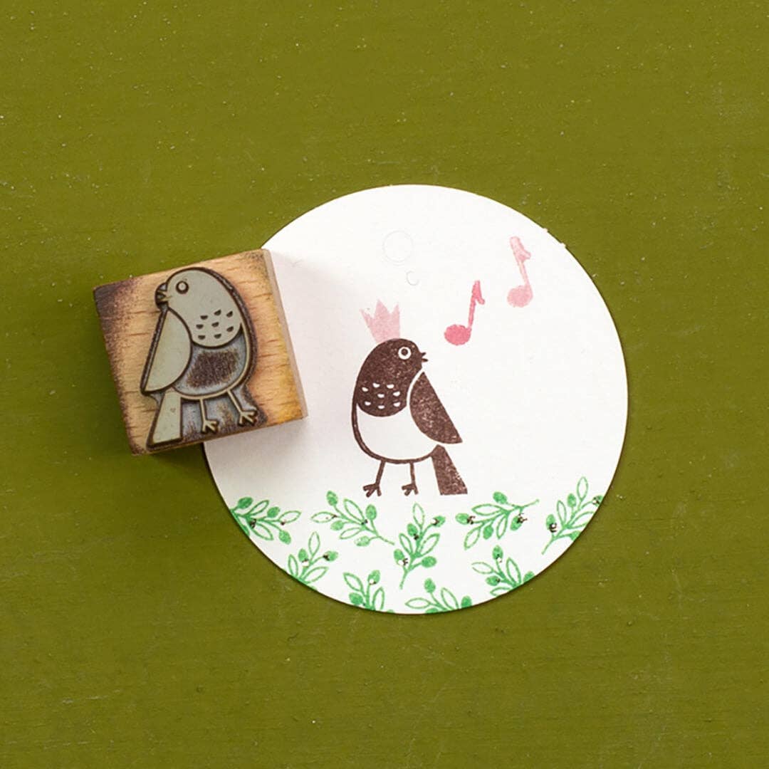 Wooden stamp with a bird design on a round white card with a printed design on a green background