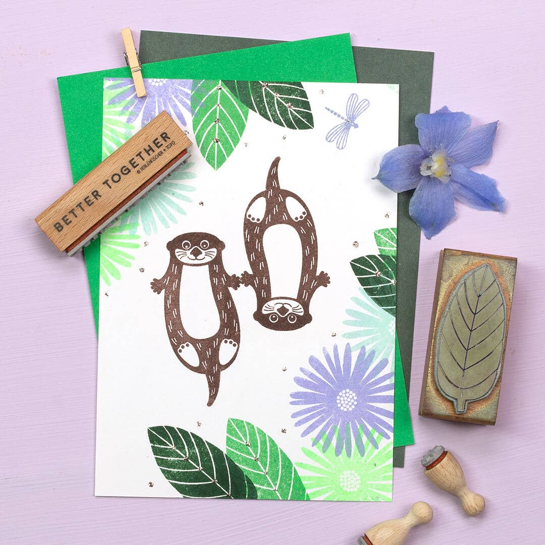 Card with otter illustrations and stamps on a purple background
